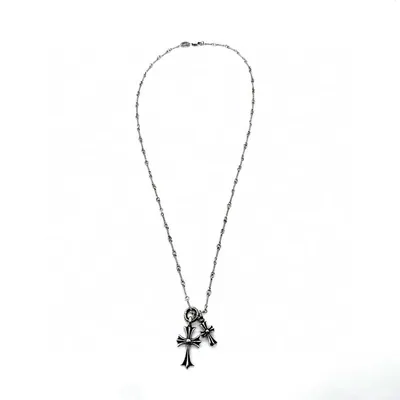 A silver chain necklace laid flat on white, with small beads spaced evenly along the links. A toggle ring near the bottom carries two flared crosses, one larger than the other, each with a darkened centre.